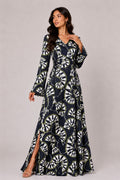 Woman wearing a long, patterned dress against a plain background