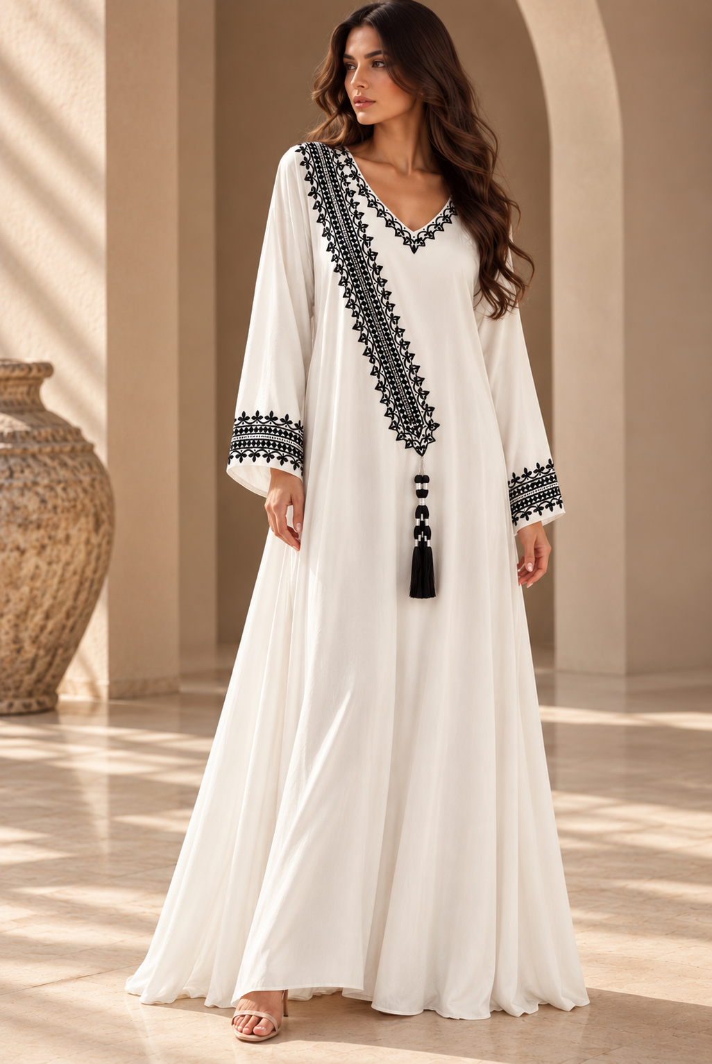 White full-length cotton dress with black hand embroidery, a V-neck, diagonal embroidered panel, long sleeves and tassel.